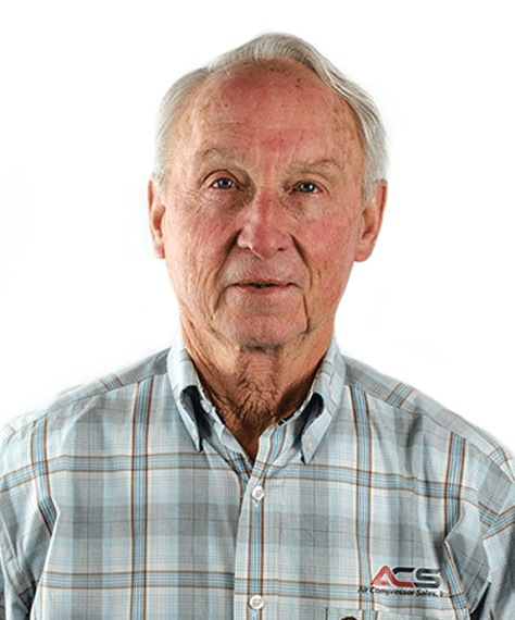An older man with short gray hair wearing a light plaid button-up shirt with an ACS logo, standing against a plain white background.