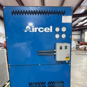 A large blue industrial machine labeled Aircel with four gauges, a control box, and cables in a warehouse with metal roof beams.
