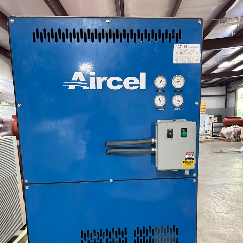 A large blue industrial machine labeled Aircel with four gauges, a control box, and cables in a warehouse with metal roof beams.