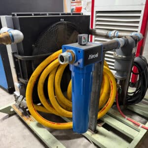 A blue Aircel air filter connects to black pipes, with big yellow hoses coiled behind it on a pallet inside an industrial workshop.
