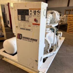 A white industrial air compressor labeled Gardner Denver Electra-Saver II sits on a warehouse floor with visible labels and control panel.